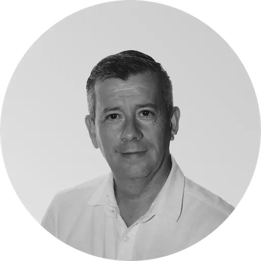 Portrait en noir et blanc d'un homme en chemise blanche, souriant doucement sur un fond uni. Le ton est calme et professionnel.