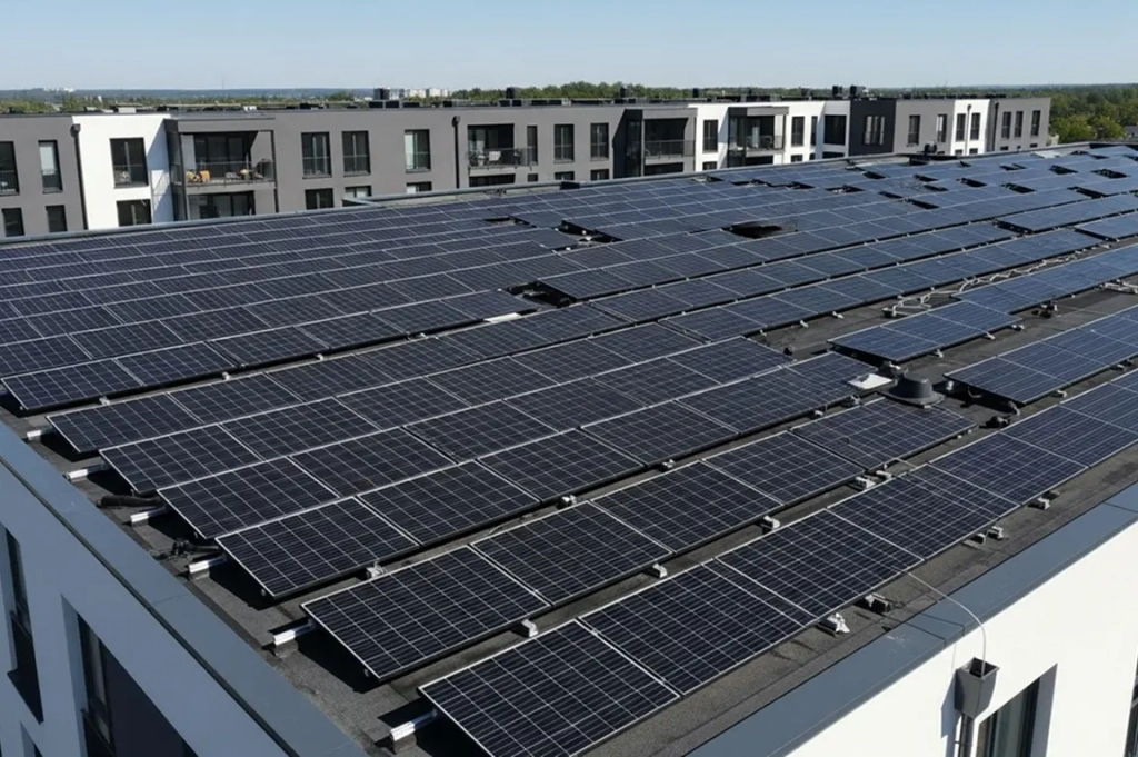 Panneaux solaires sur le toit d'un immeuble moderne sous un ciel bleu clair, avec des immeubles d'appartements gris et blancs identiques en arrière-plan.