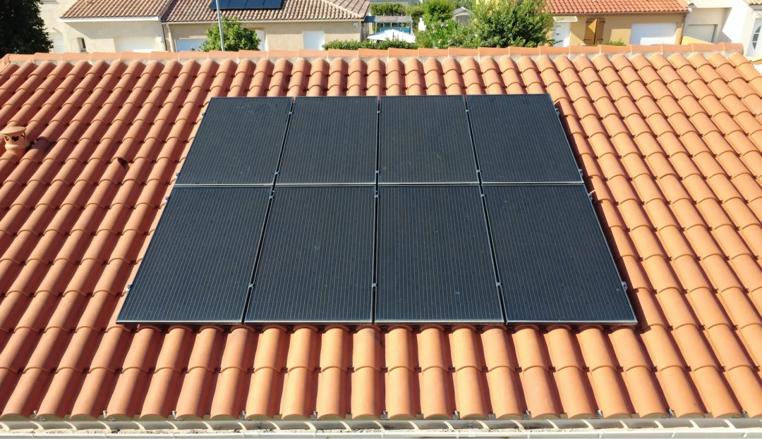 Toiture avec six panneaux solaires sur tuiles en terre cuite orange. Les panneaux sont centrés, entourés d'arbres et de maisons verdoyantes, reflétant une utilisation durable de l'énergie.